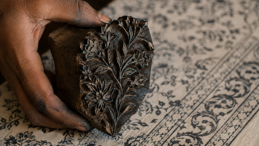 Dye-stained hand-carved wooden printing block held above block-printed cotton, showing the floral pattern cut in relief, how block printing is done, House of Falguni