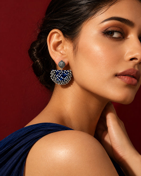 Blue chandbali earrings worn on a model in a navy drape against a deep maroon ground (AI-generated styling image)