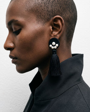 Profile of a woman in a dark high-collared jacket wearing the Black Bloom tassel earring with a pearl cluster