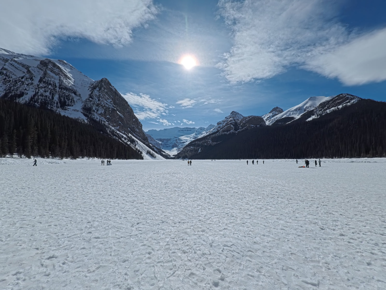 Frozen Lake Louise under snow, ringed by dark spruce and grey mountains at the turn of spring in Banff