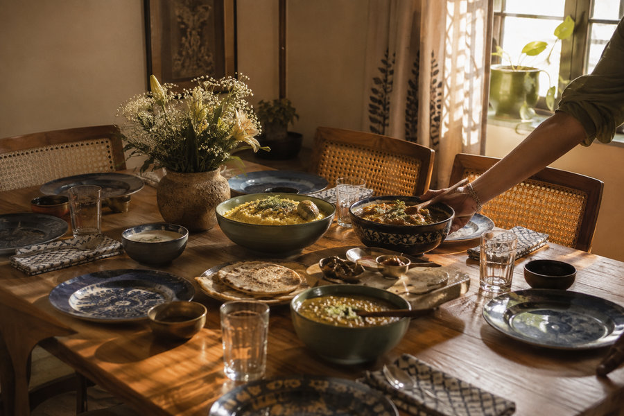 An Indian dinner table set with hand-painted blue ceramic plates and bowls of khichdi, curry, dal and roti, wildflowers in a stoneware vase, warm evening light — how to host an Indian dinner party, House of Falguni