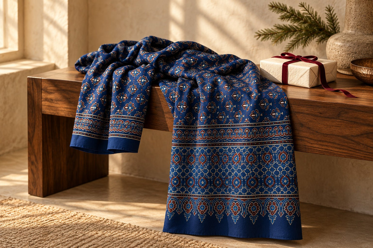 An indigo Nilufar Ajrakh stole folded beside a loosely tied gift in warm December light.