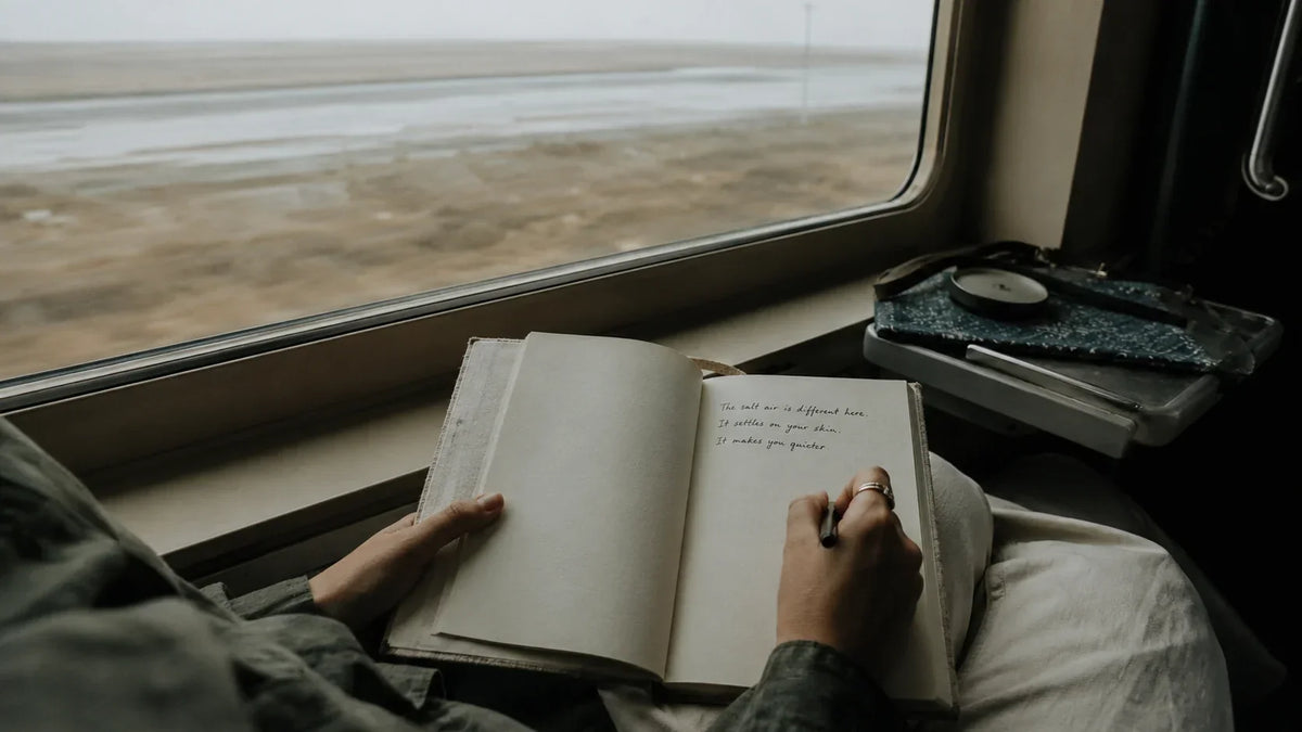 Hands writing a short entry in a fabric diary on a train crossing the Rann of Kutch with salt flats through the window, how to keep a travel journal, House of Falguni