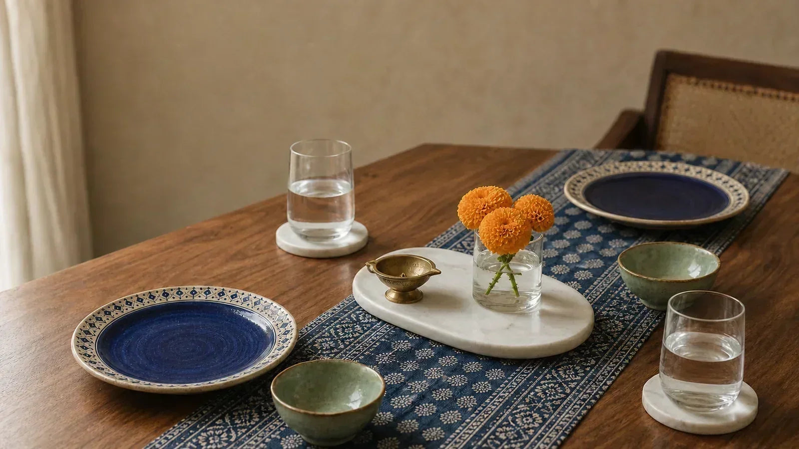 An Indian dining table styled with hand-painted indigo ceramic plates, sage green katoris and marble coasters on warm wood