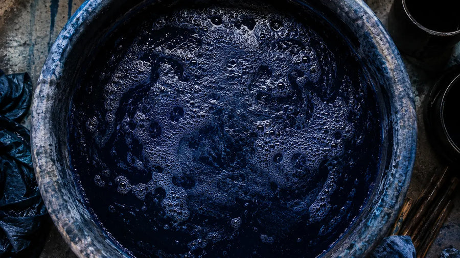 An indigo dye vat photographed from directly above, deep blue-black with a coppery froth across the surface