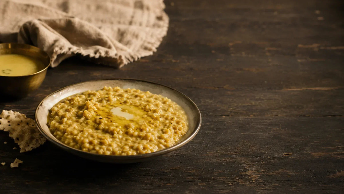 A bowl of moong dal khichdi with ghee pooled at the centre, served with a brass bowl of kadhi and roasted papad