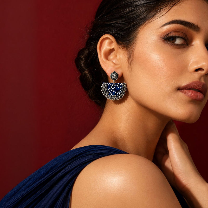 Model in a navy drape wearing the Blue Chandbali earrings, a fabric-covered base with kundan and ghungroo detail, against a crimson wall: handmade jewellery by House of Falguni