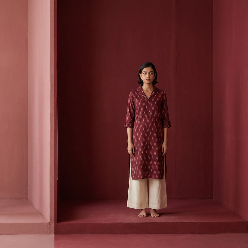A woman in a maroon kurta with an ikat collar standing in a maroon painted room