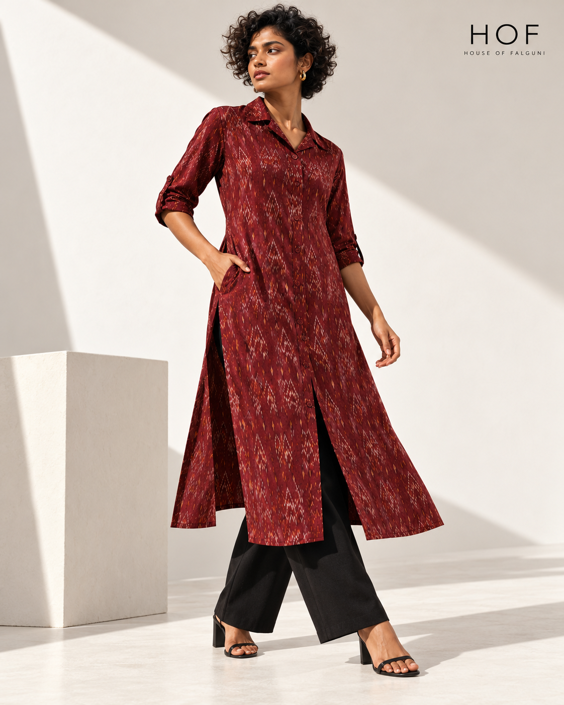 Ruby Raga maroon ikat collar kurta with rolled sleeves and front slits, worn with black trousers in a sunlit white studio (AI-generated styling image)