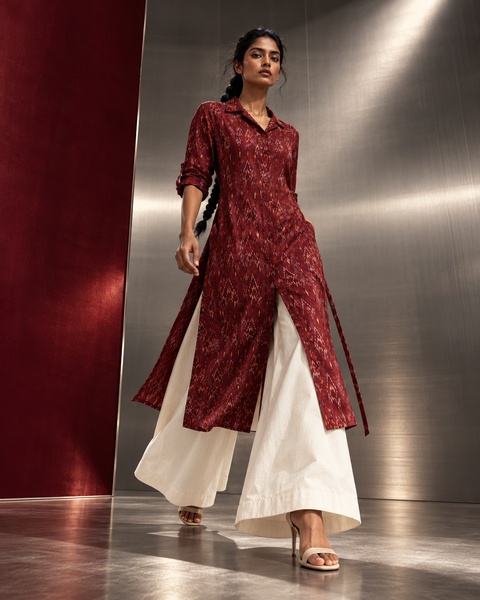 Ruby Raga maroon ikat collar kurta with long front slits, worn over wide white palazzo trousers against brushed steel walls (AI-generated styling image)