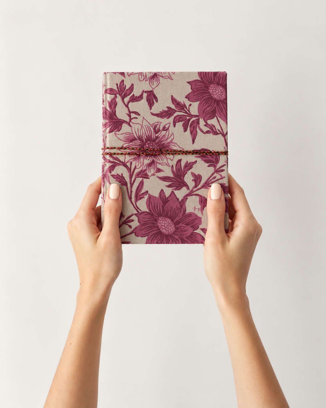 Blush Garden block print fabric diary held up in both hands against a pale wall, plum-pink flowers on ivory