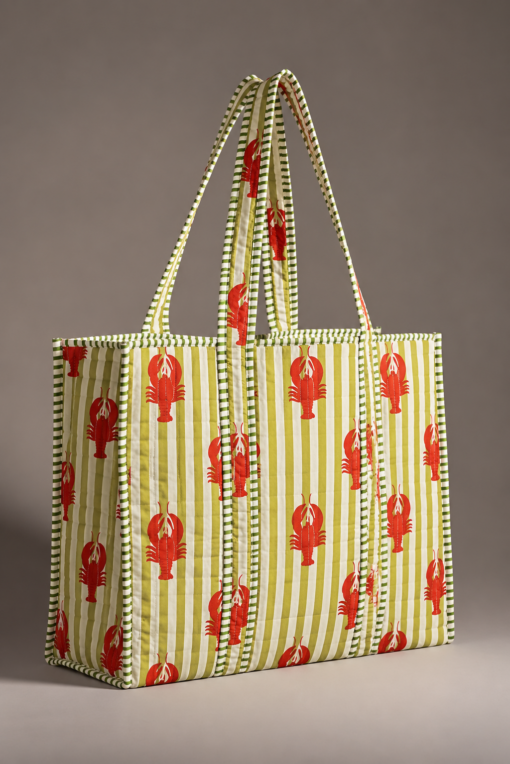 Aakar red lobster stripe quilted tote standing upright, showing the green striped binding and handles