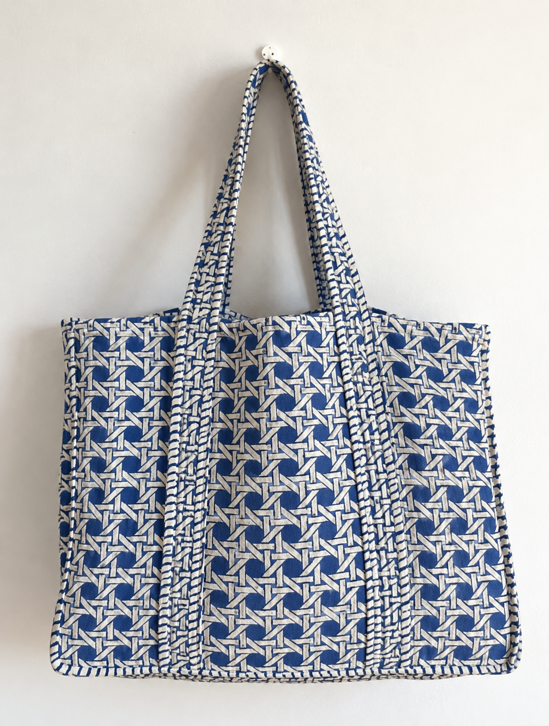 Samudra large quilted tote in a blue and white cane-weave print, hanging flat against a white wall