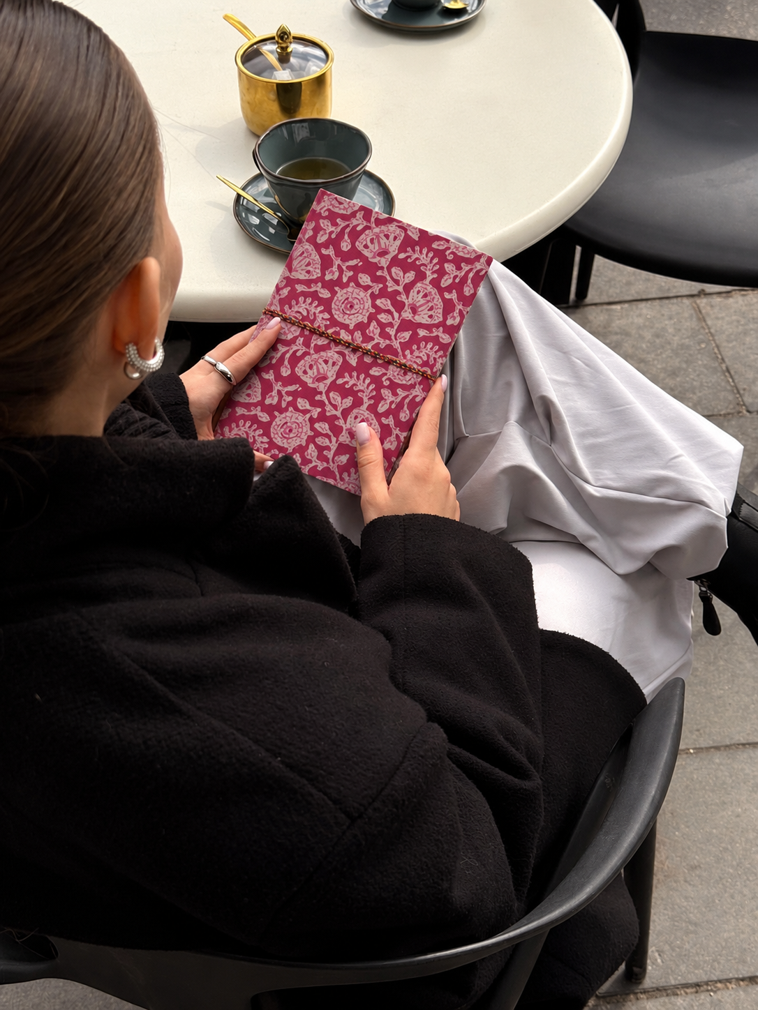 Pink block print fabric diary with dense pale florals, read at a café table with a cup of green tea