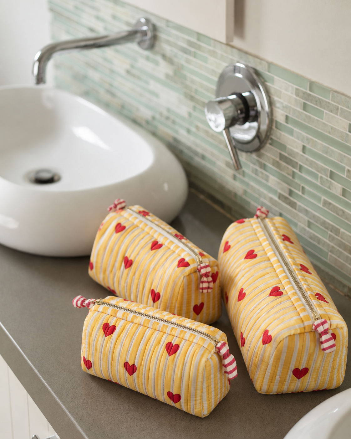 Sunehri quilted makeup pouch set of three in yellow stripes with small red hearts, on a bathroom counter