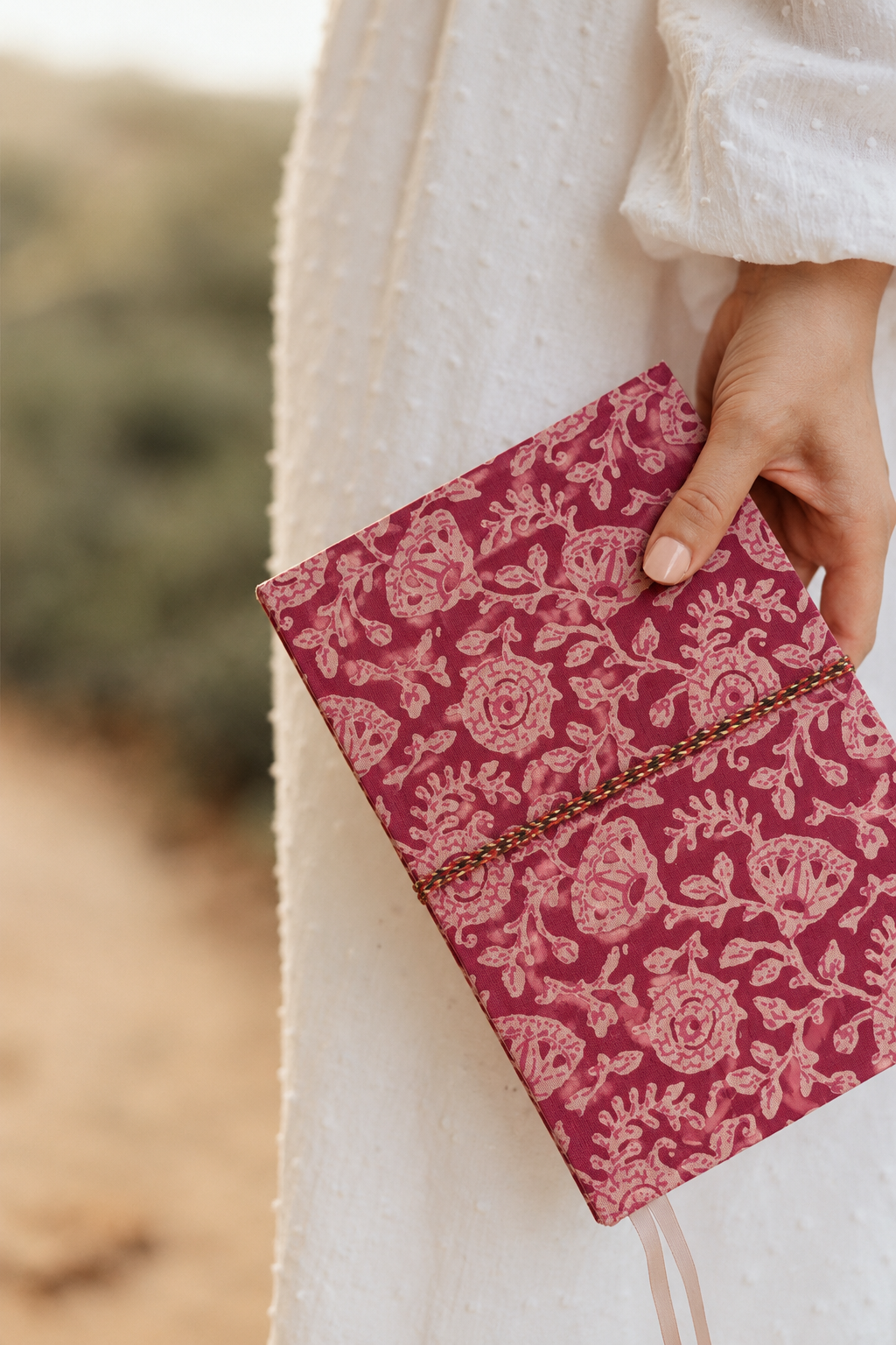 Pink block print fabric diary with dense pale florals, held at the side against a white dotted dress