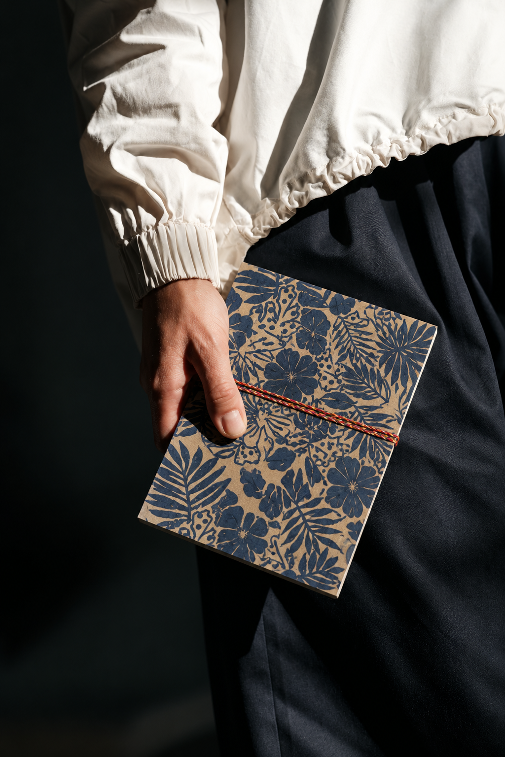 Indigo Tropics block print fabric diary held at the hip against black trousers and a cream jacket