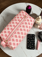 Gulaab quilted hair tool bag in a red buti print on pale pink, zipped shut on a marble table