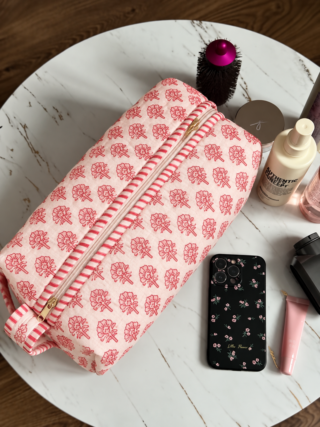 Gulaab quilted hair tool bag in a red buti print on pale pink, zipped shut on a marble table