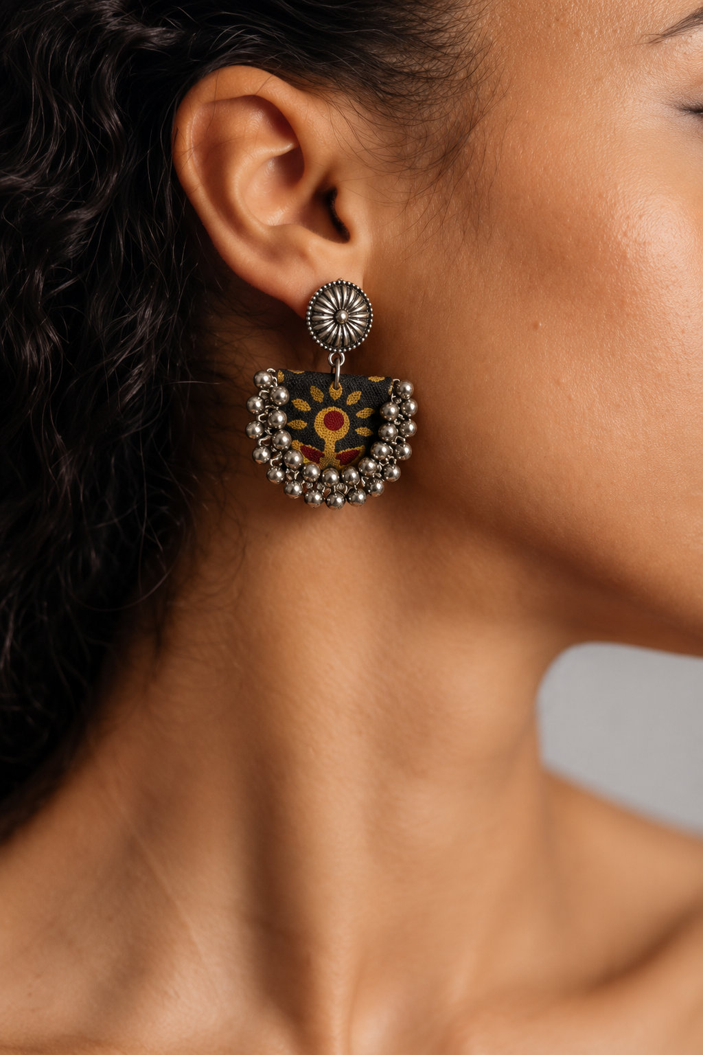Close-up of a Black Chandbali Earring on the ear: kundan top over a black fabric crescent printed with mustard flowers, edged with ghungroo bells