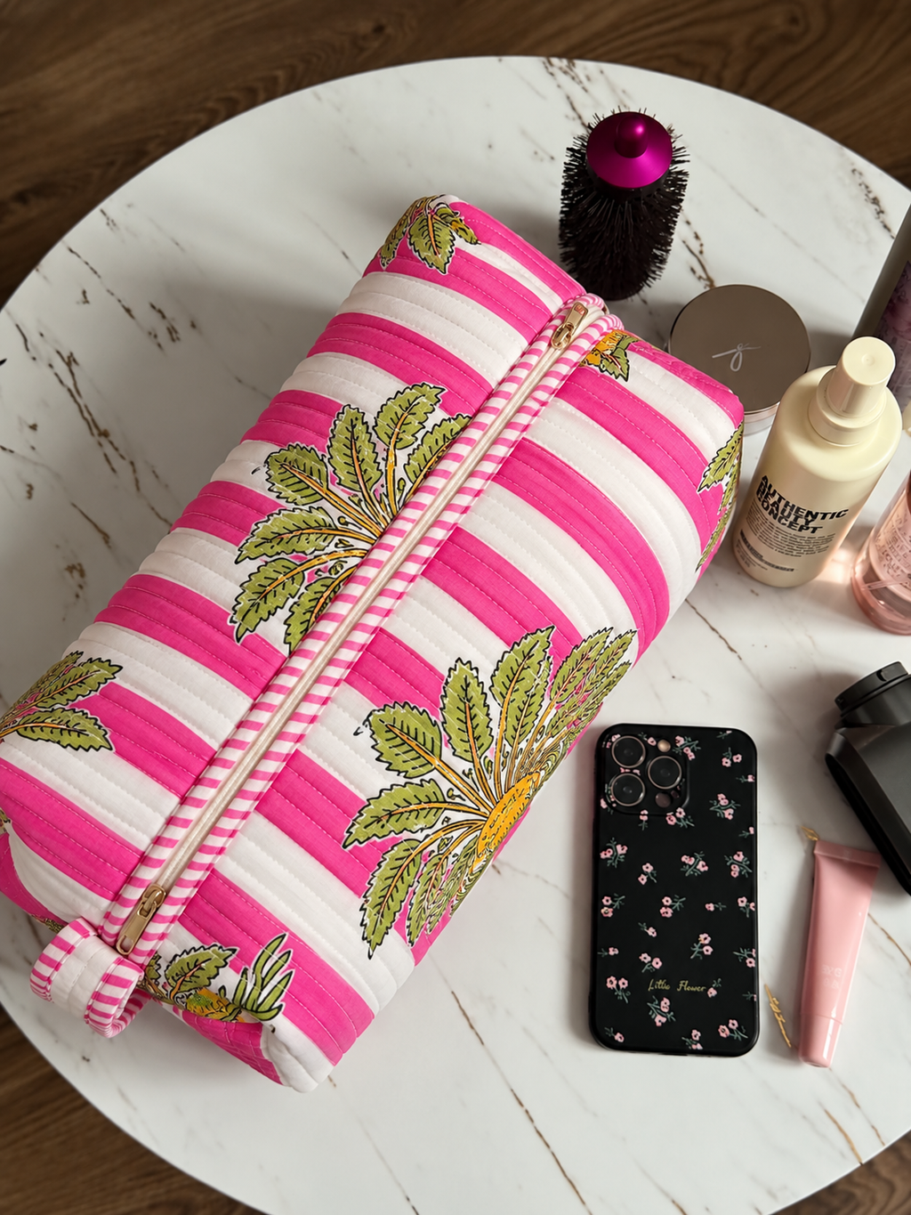 Gul pink stripe quilted hair tool bag zipped shut on a marble table beside a round brush, phone and skincare