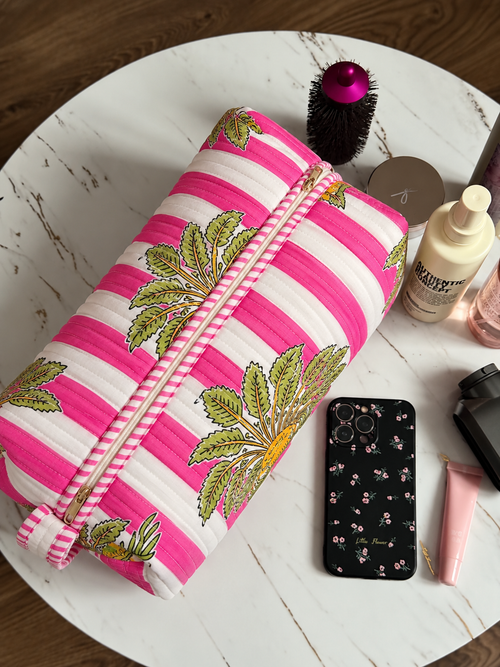 Gul pink stripe quilted hair tool bag zipped shut on a marble table beside a round brush, phone and skincare