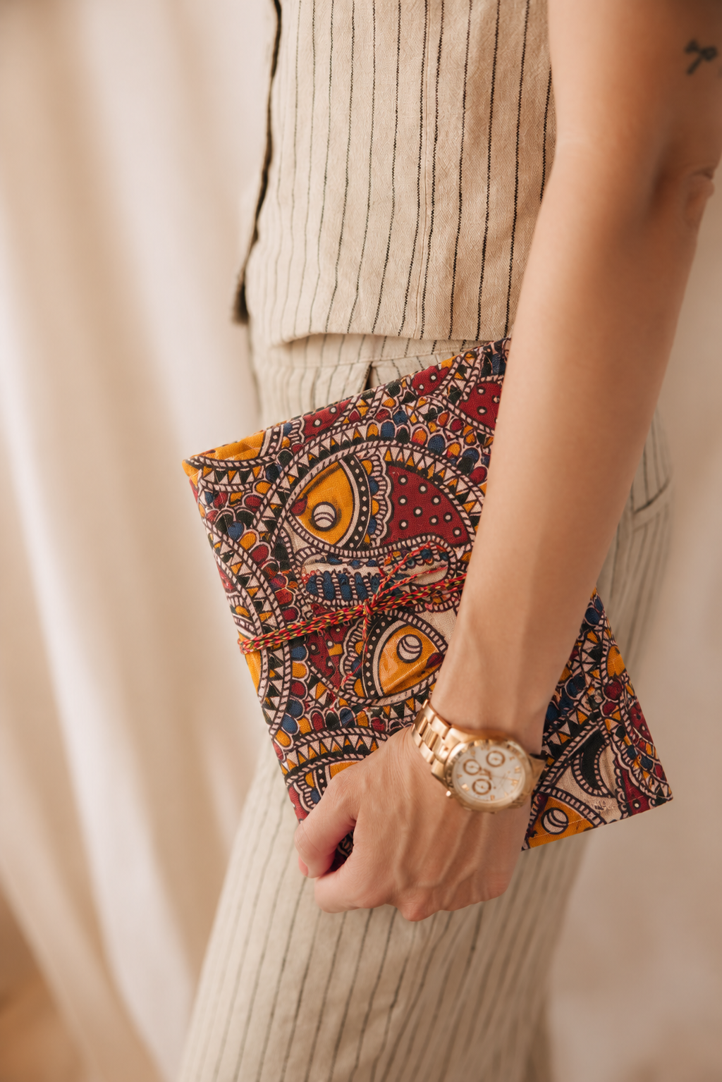 Madhubani Carnival block print fabric diary held at the side against cream pinstriped trousers, gold watch on the wrist