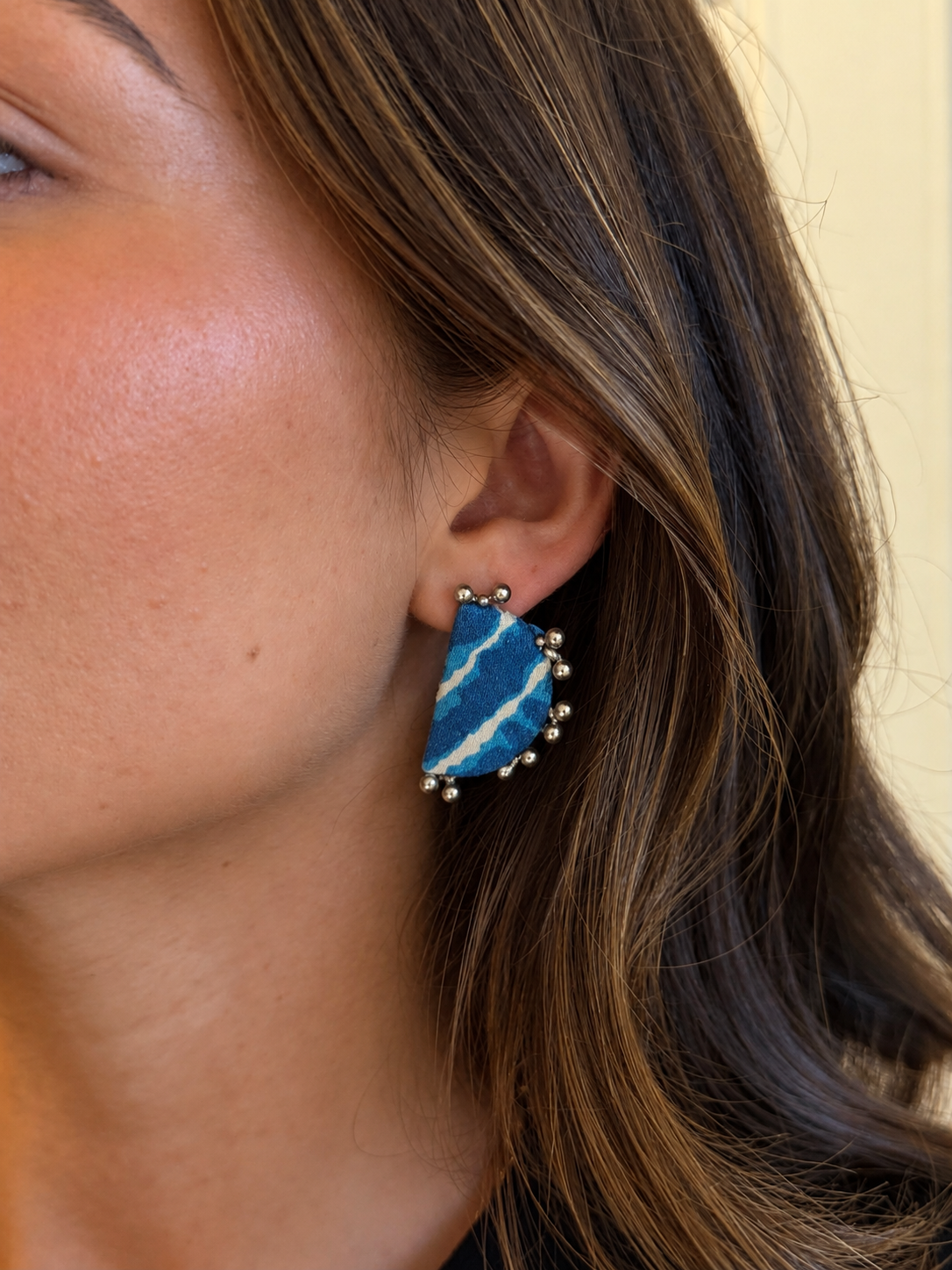 Close-up of a Leher Sky Blue half moon earring on the ear: sky blue and white lehariya stripes with ghungroo bead points