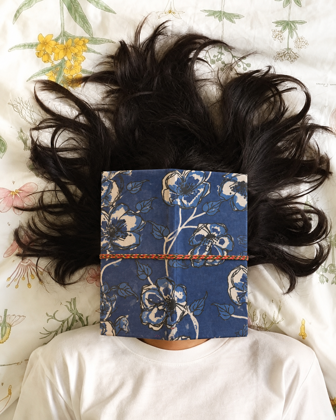 Neela Phool block print fabric diary resting over the face of someone lying on floral bedding, dark hair fanned out