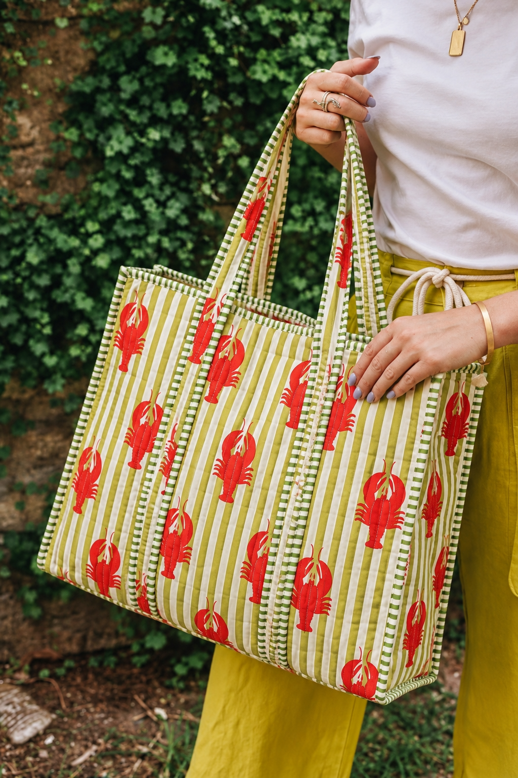 Aakar red lobster stripe quilted tote carried by hand outdoors, showing the green-and-white striped handles