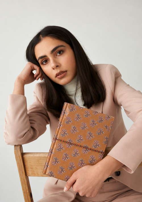 Amber Buti block print fabric diary held on the knee by a woman in a blush pink suit, seated on a wooden chair