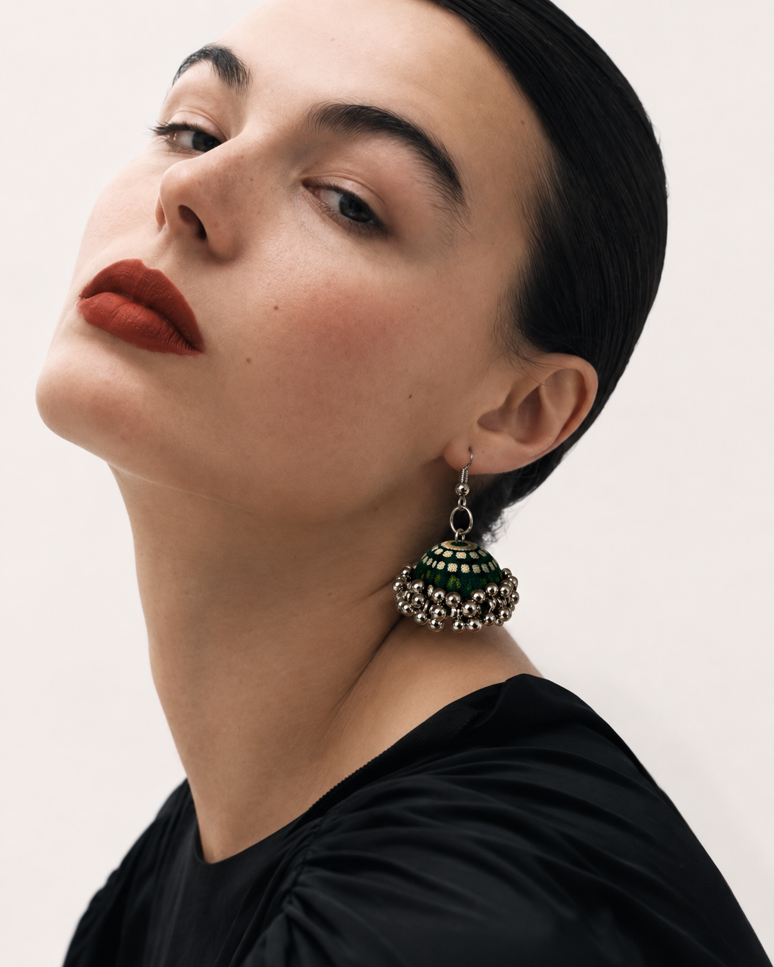 Green striped fabric jhumka worn with a black top and a red lip, head tilted back