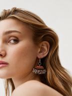 Rust-orange jhumka against blonde hair with sea and sky behind