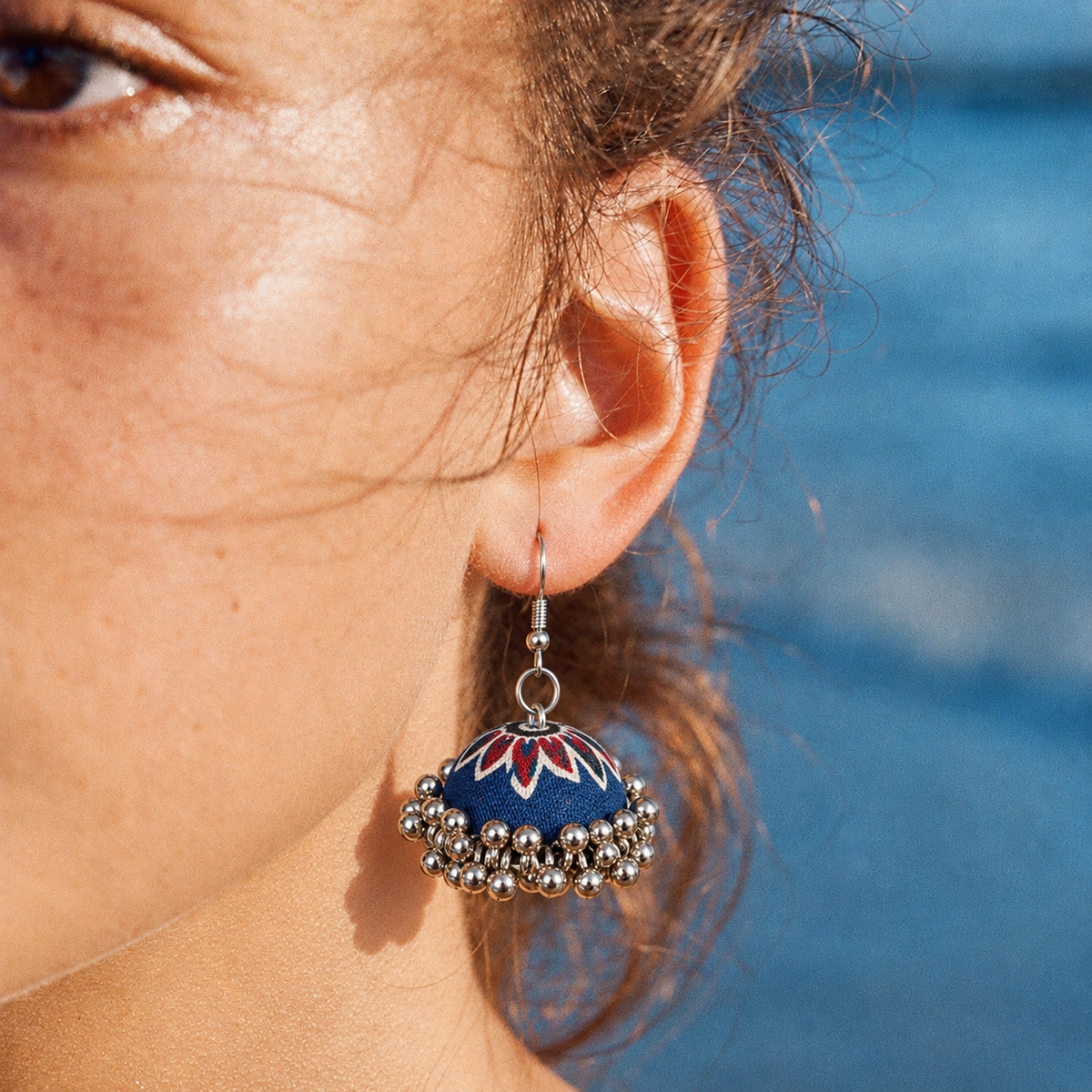 Laalbagh jhumka worn by the sea, sunlight across the navy and red fabric dome