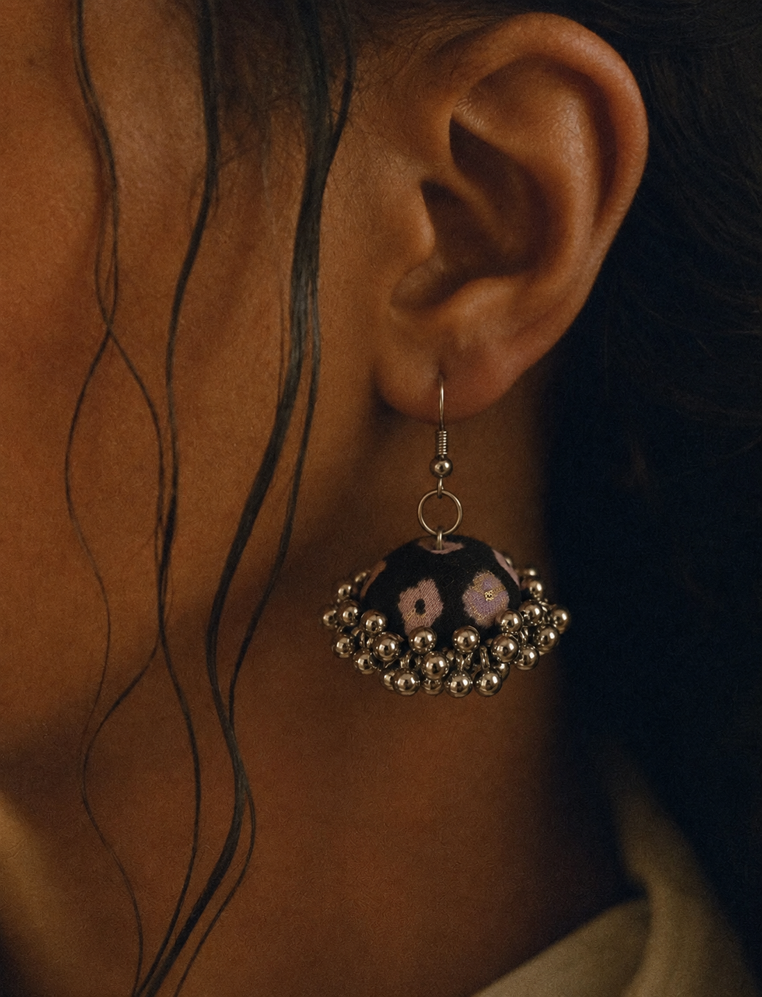 Vanraaj jhumka in low warm light, dense silver bead fringe below the black fabric dome
