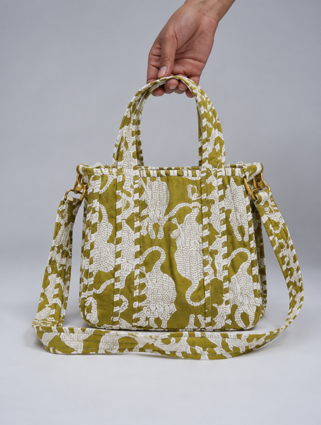 Matsya quilted mini tote in olive green with a white big cat print, held by its top handles with the strap attached
