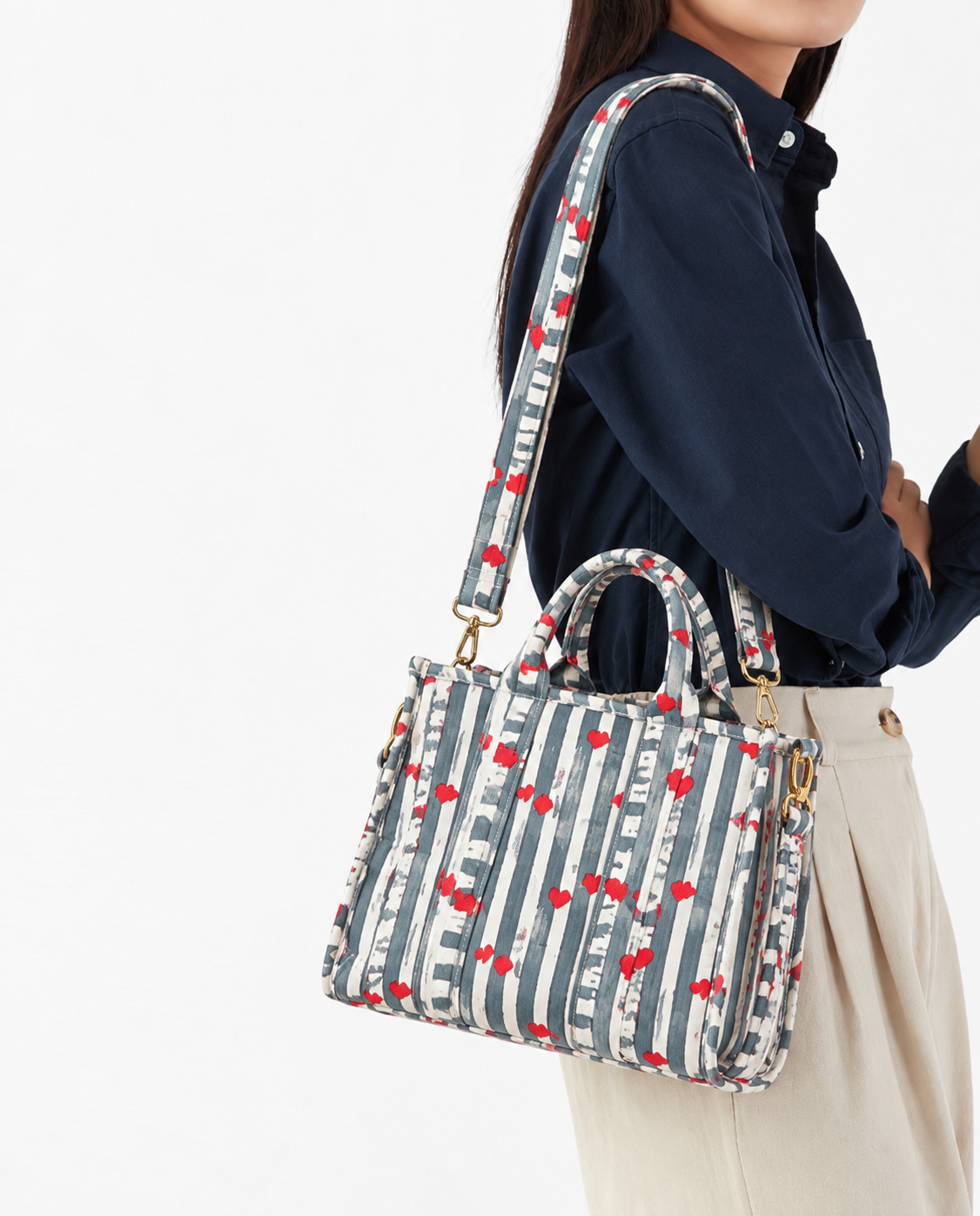 Jal grey stripe mini tote worn over the shoulder on its long strap, showing the gold-tone snap hooks