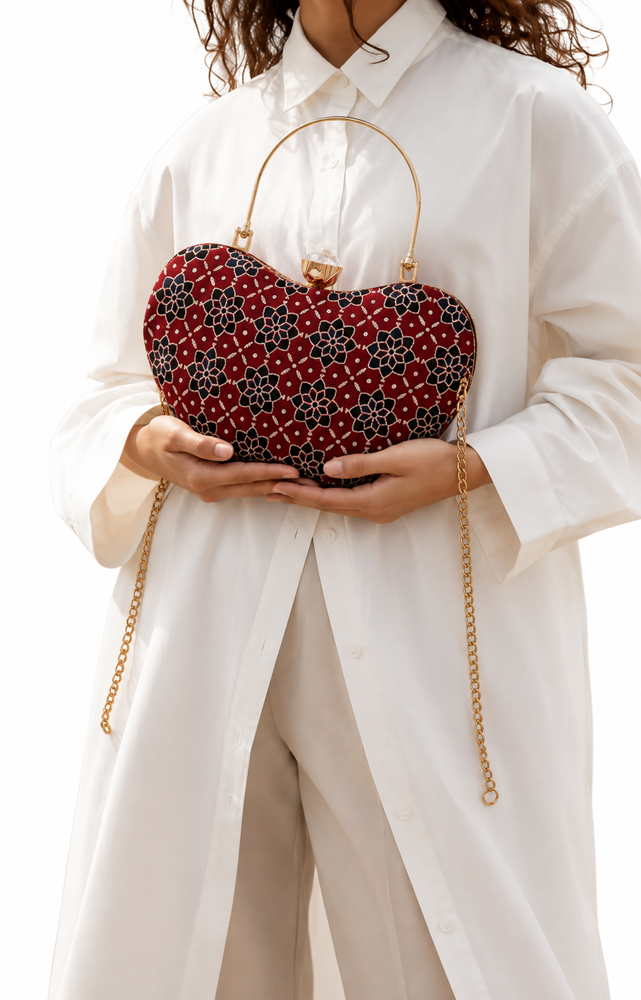 Laal Noor red floral Ajrakh block-print Mashru silk handbag held against a white shirt, gold-tone arched handle and jewelled clasp, House of Falguni