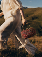 Rang Mahal red floral Ajrakh block-print Mashru silk handbag carried by hand, model walking through grassland, House of Falguni