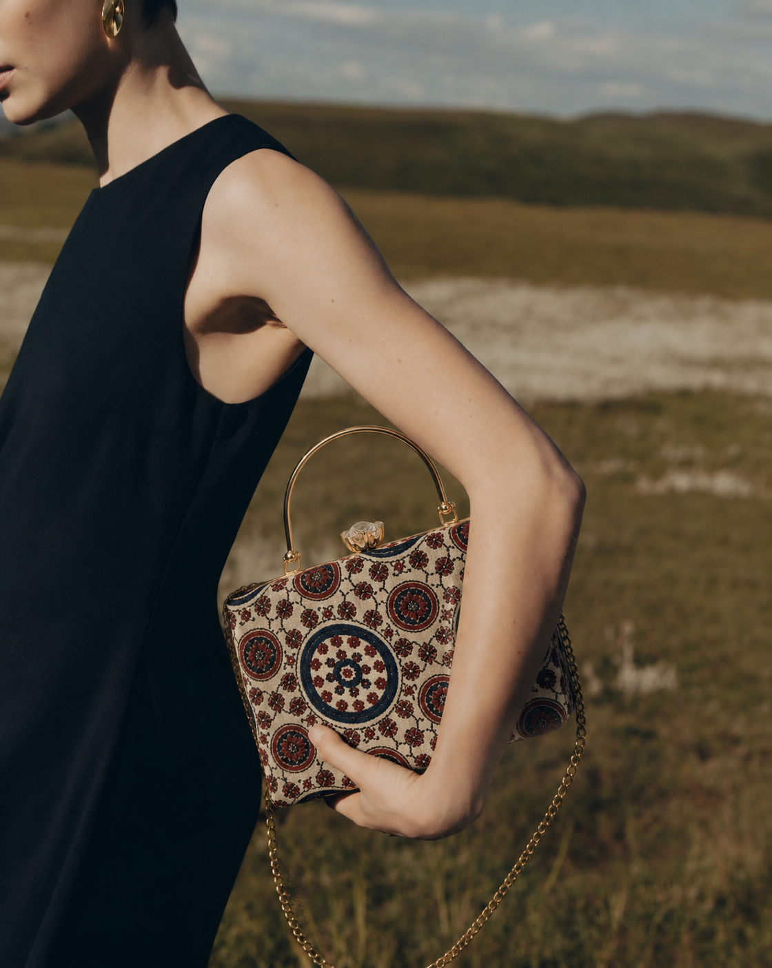 Aaina ivory and navy Ajrakh block-print Mashru silk handbag with medallion pattern, held against a black dress, House of Falguni