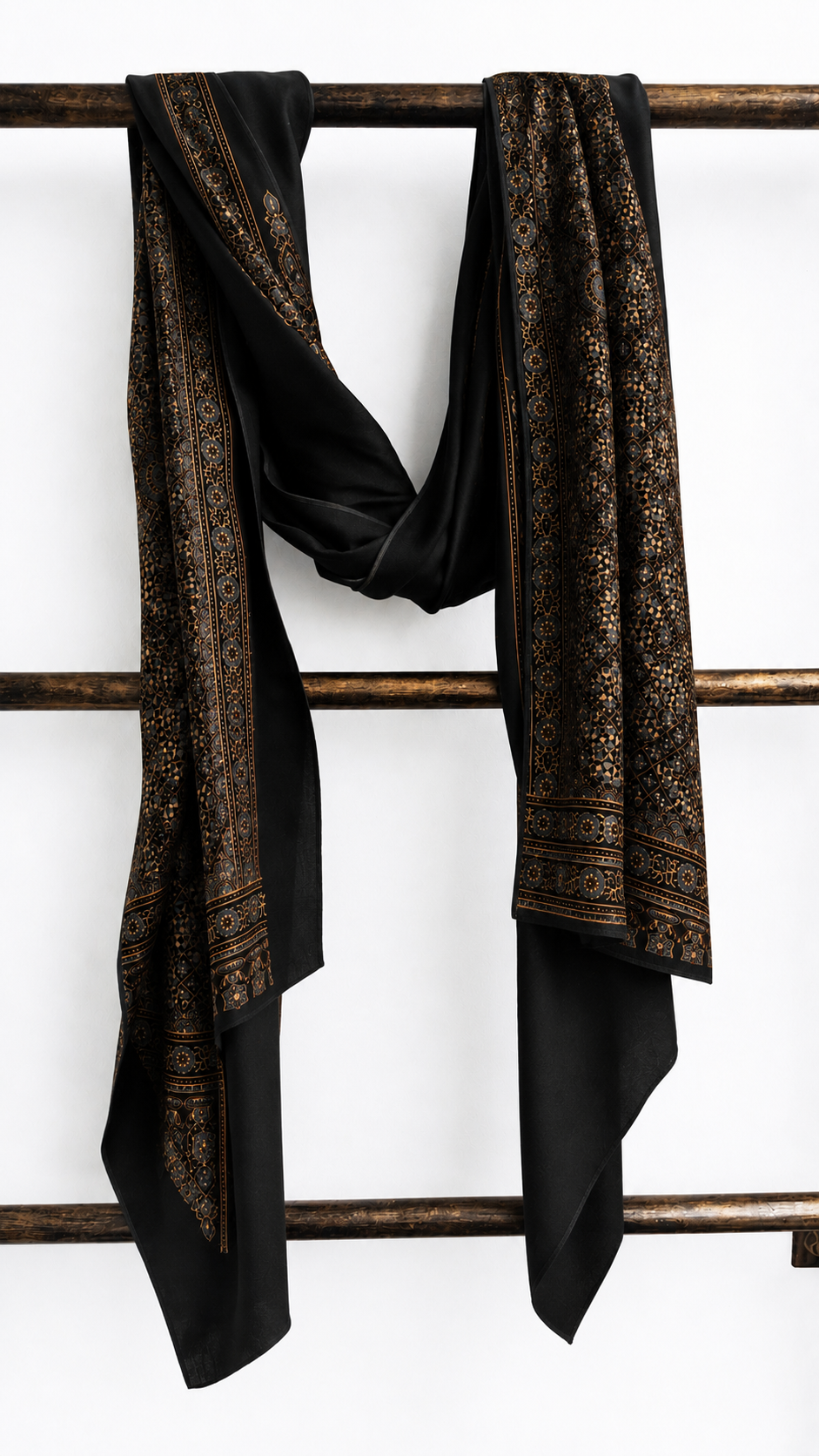Shahi Ajrakh black modal silk stole hung on a wooden ladder, showing its hand block-printed border