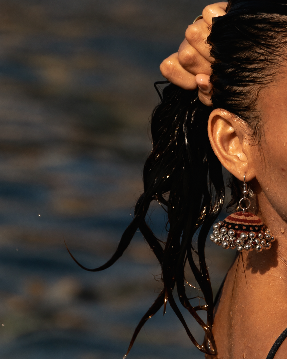 Rust-orange fabric jhumka earring with silver beadwork, worn by the water — House of Falguni