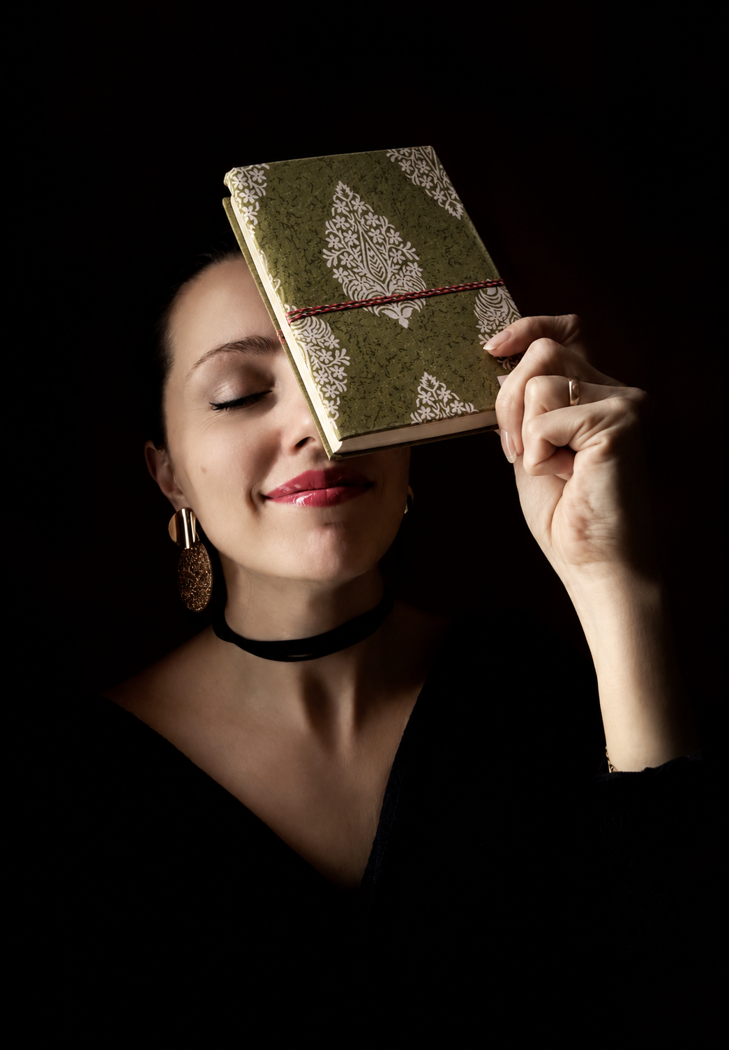Olive Dabu block print fabric diary held against the brow, eyes closed, black top and velvet choker on a dark background