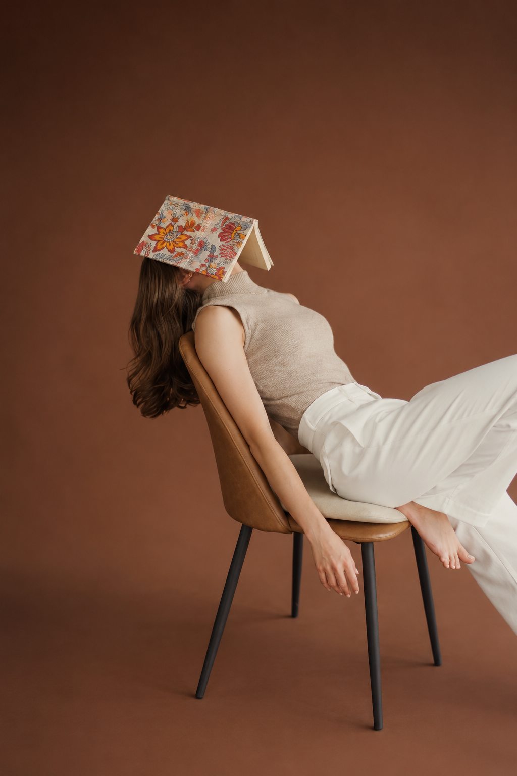 Hara Mahal block print fabric diary resting open over the face of a woman reclining on a tan chair, brown backdrop