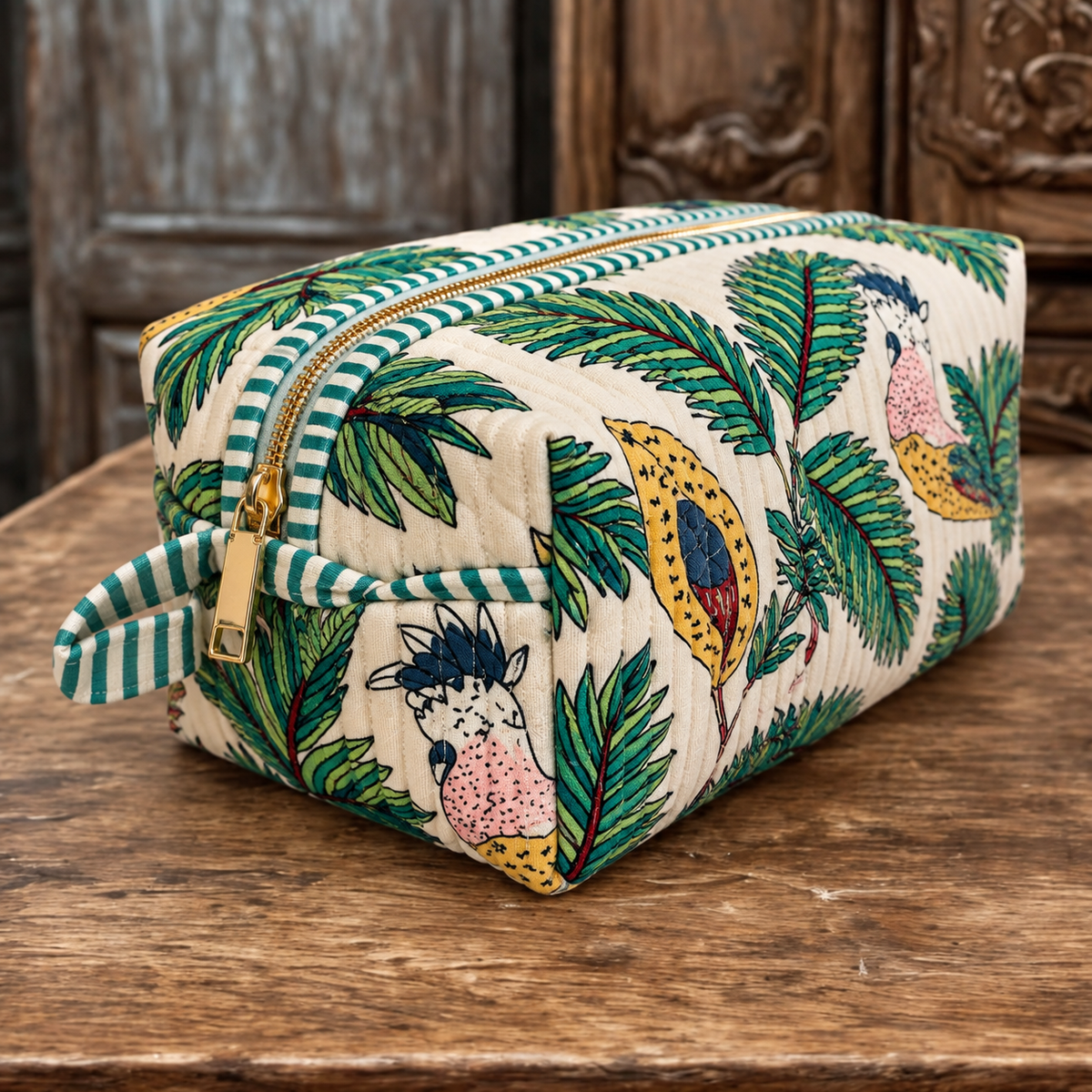 Vaan quilted hair tool bag in cockatoo and palm print, zipped shut, showing the gold zip and green striped end handle