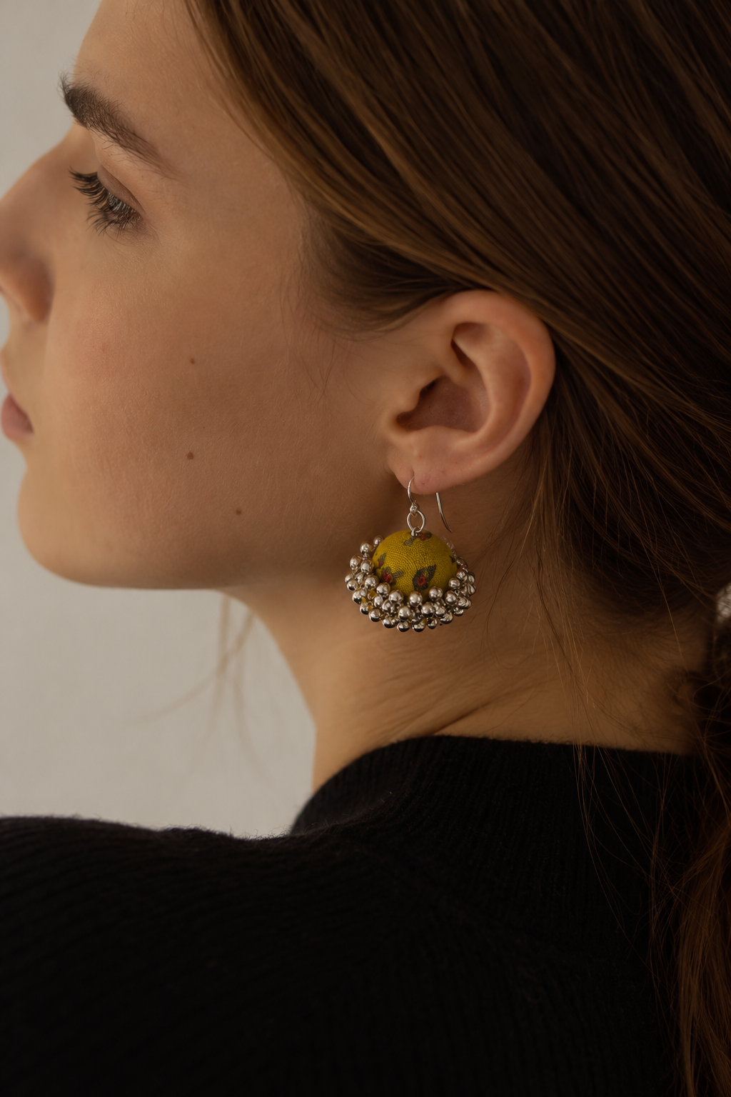 Mustard fabric jhumka earrings in profile with a black top: mustard dome with olive and grey leaf motifs and ghungroo bells