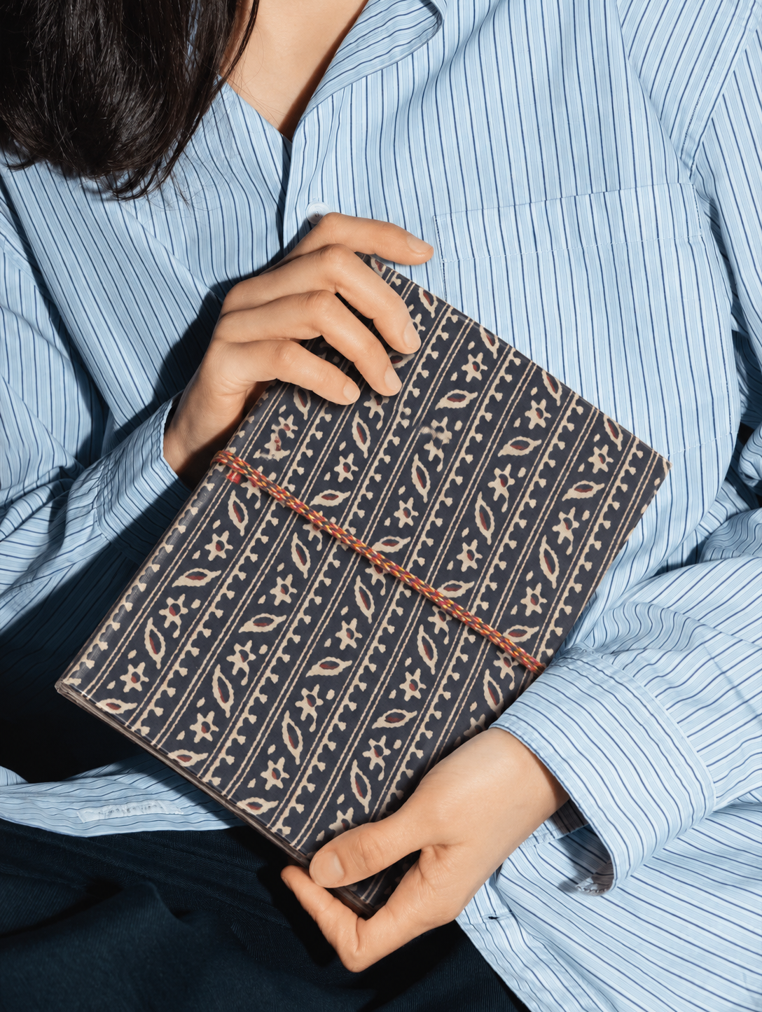 Indigo Ajrakh block print fabric diary held against a blue and white striped shirt