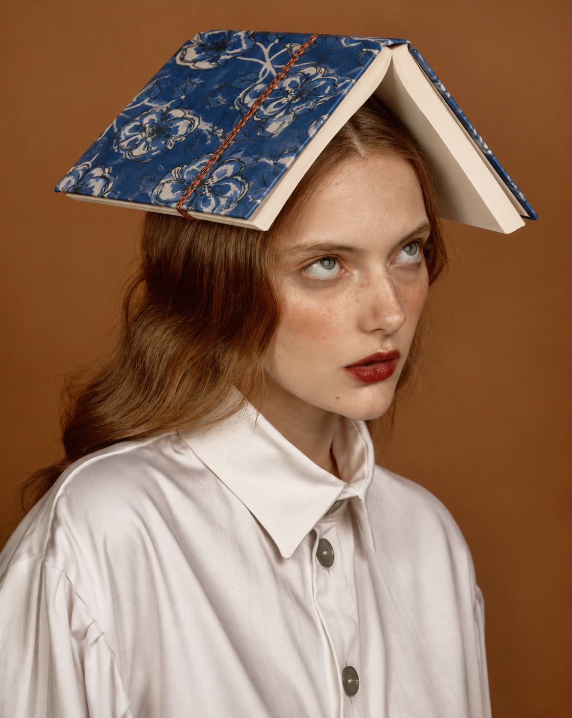 Cobalt blue block print fabric diary with large white-outlined flowers, balanced open on the head of a woman in a white shirt