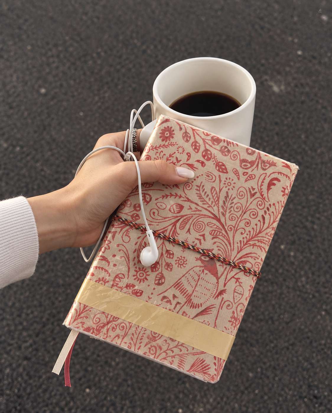 Crimson Peacock block print fabric diary held over a cup of black coffee, white earphones looped around the fingers