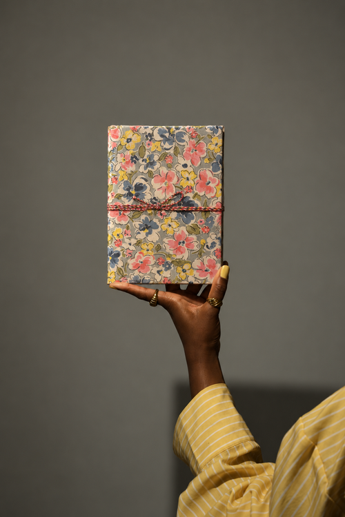 Bahar Medley block print fabric diary raised in one hand against a grey wall, yellow striped sleeve